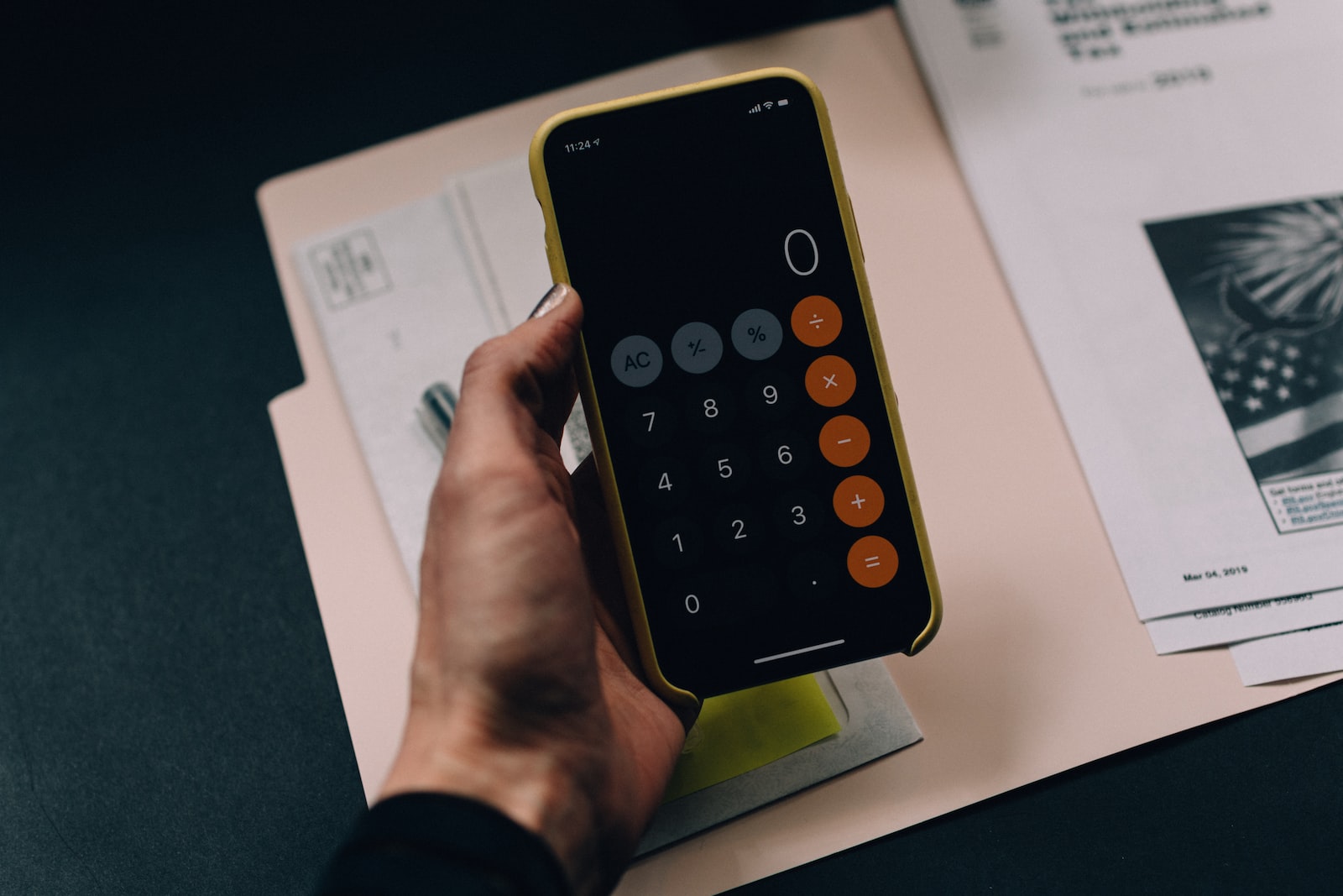 iPhone open to calculator app being held in a person's hand above a manila folder of paperwork