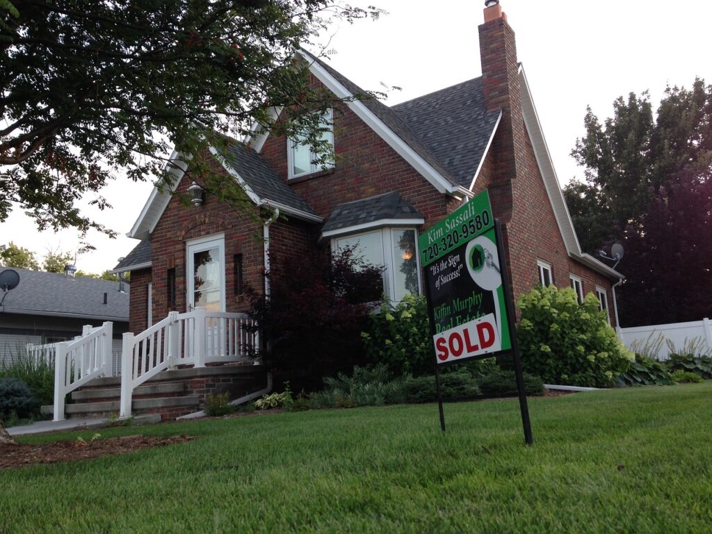 red brick home with white trim and green grass with sold sign in yard