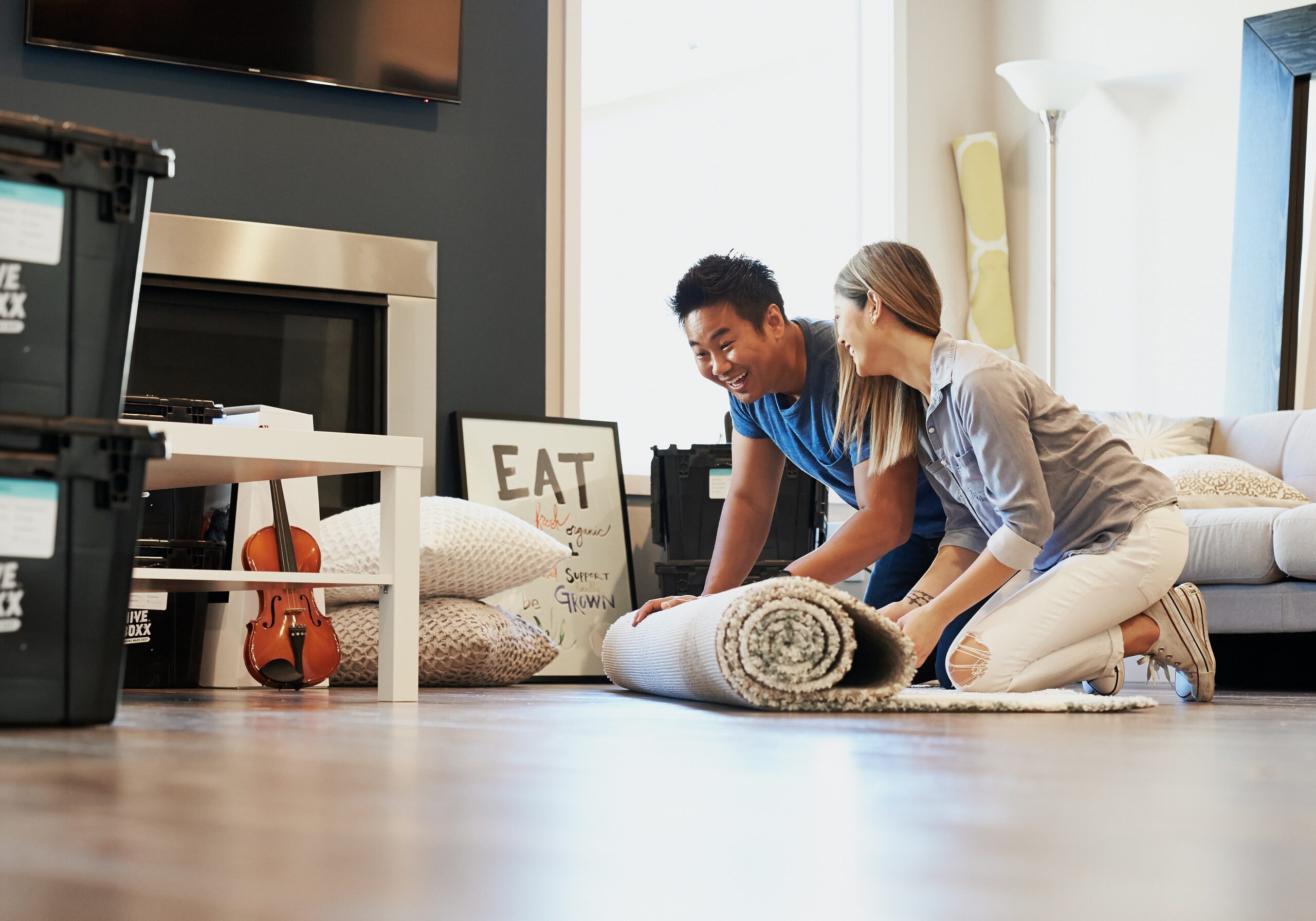man in blue shirt and woman in sweater unrolling a rug on a wooden floor