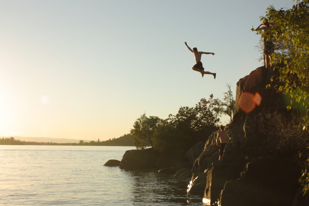 person diving from cliff to body of water during sunset in Montana