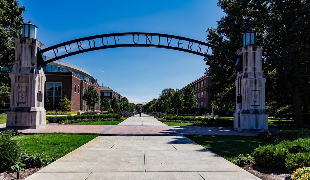 Iron archway that says Purdue University stretching over a sidewalk against a blue sky